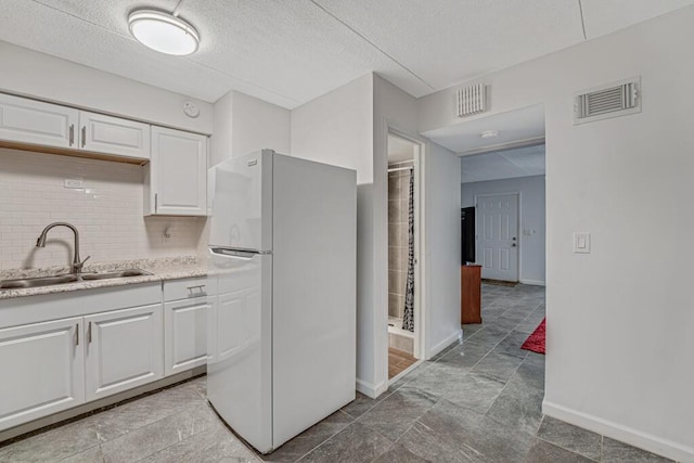 kitchen featuring freestanding refrigerator, white cabinetry, a sink, and visible vents