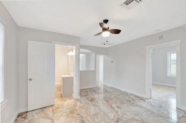 unfurnished room with a ceiling fan, arched walkways, visible vents, and baseboards