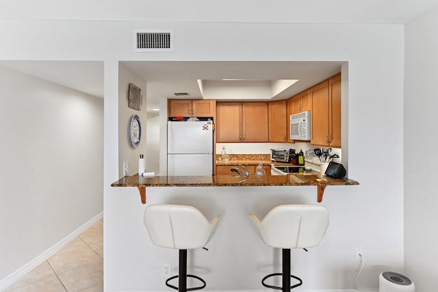 kitchen featuring dark stone counters, white appliances, and a kitchen breakfast bar