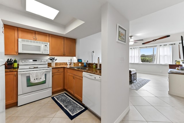 kitchen with white appliances, a skylight, ceiling fan, light tile patterned flooring, and a raised ceiling