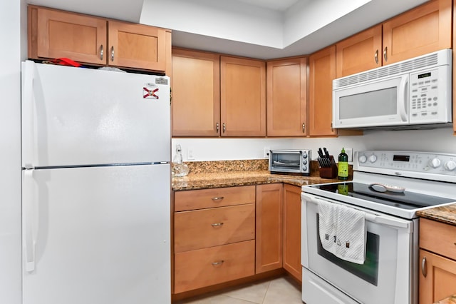 kitchen with dark stone counters, white appliances, and light tile patterned floors