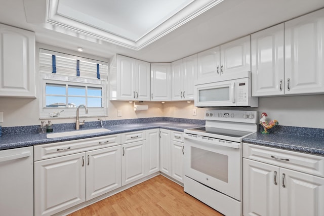 kitchen featuring a sink, a tray ceiling, dark countertops, white appliances, and white cabinets