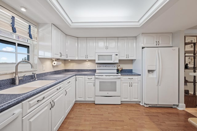 kitchen with white appliances, dark countertops, a tray ceiling, and a sink