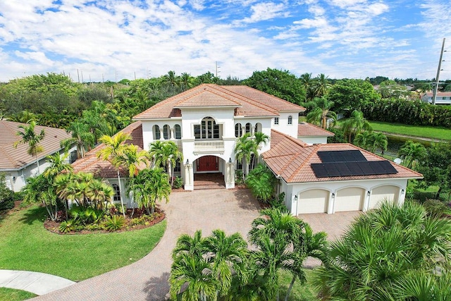 mediterranean / spanish home with a balcony, decorative driveway, solar panels, and a tiled roof