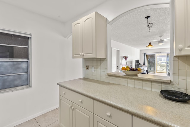 kitchen with light countertops, white cabinetry, pendant lighting, backsplash, and light tile patterned flooring