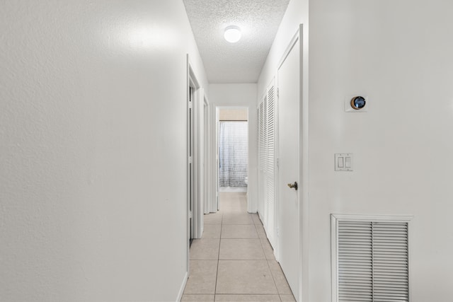 hallway featuring light tile patterned flooring, visible vents, and a textured ceiling