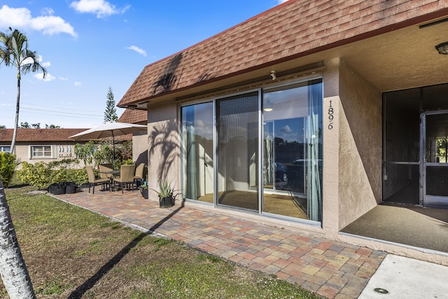 back of property featuring visible vents, mansard roof, a patio, roof with shingles, and stucco siding