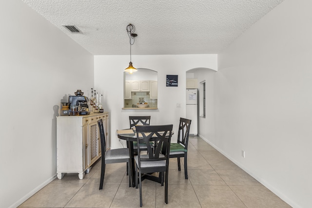 dining space featuring baseboards, visible vents, arched walkways, a textured ceiling, and light tile patterned flooring