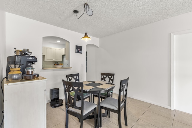 dining area featuring arched walkways, light tile patterned flooring, a textured ceiling, and baseboards