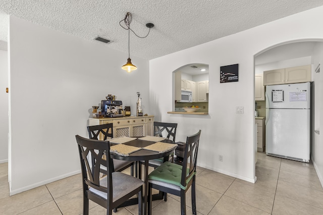 dining room with light tile patterned floors, baseboards, arched walkways, and a textured ceiling