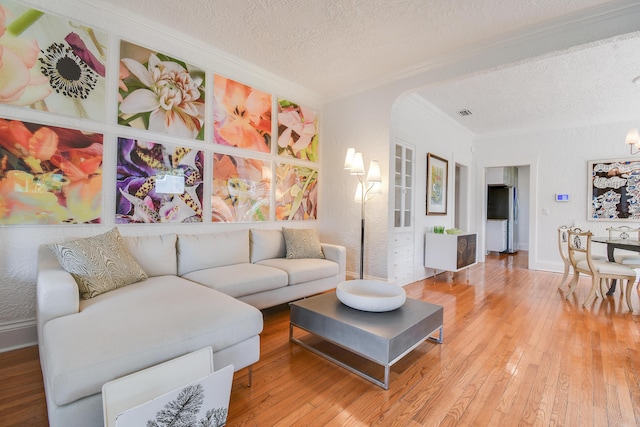 living area with crown molding, hardwood / wood-style floors, baseboards, a textured ceiling, and arched walkways