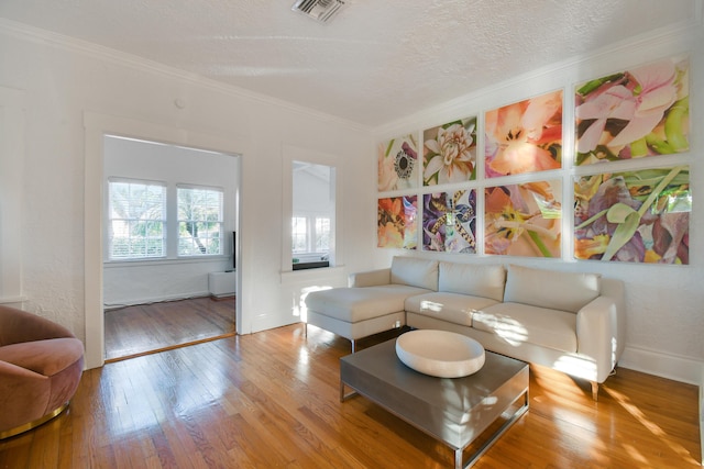 living area with crown molding, hardwood / wood-style flooring, a textured ceiling, baseboards, and visible vents