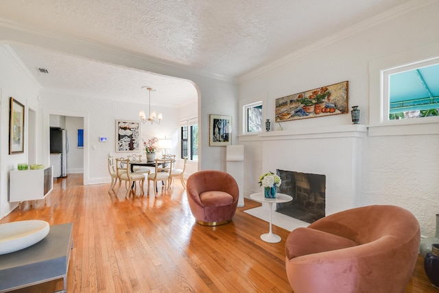 living area featuring a notable chandelier, a textured ceiling, crown molding, and light wood-type flooring