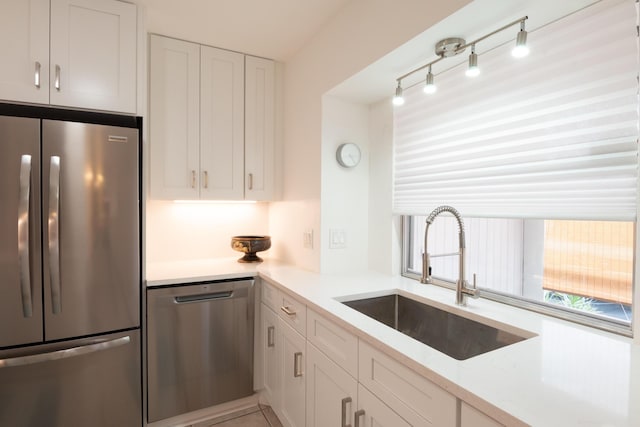 kitchen with a sink, rail lighting, white cabinetry, light countertops, and appliances with stainless steel finishes