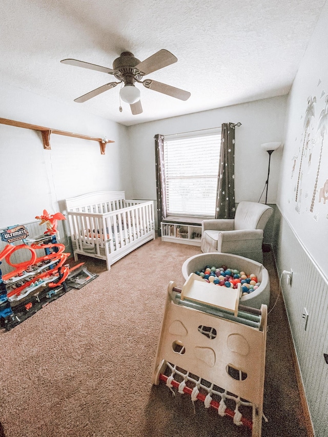 bedroom with ceiling fan, a nursery area, a textured ceiling, and carpet flooring