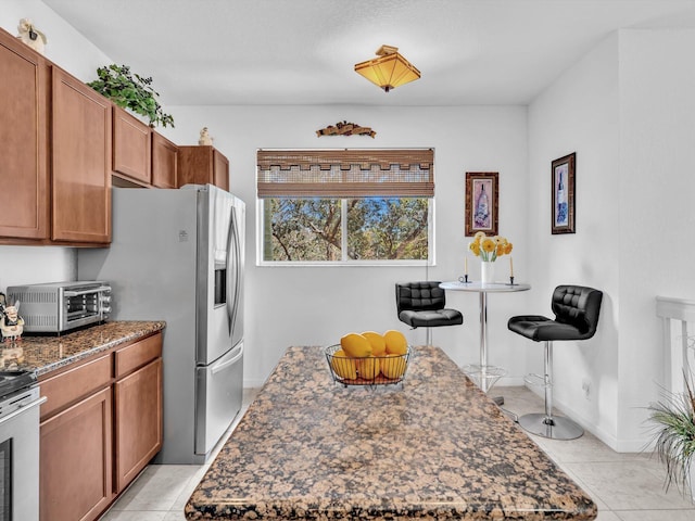 kitchen with light tile patterned flooring, stainless steel appliances, a center island, and dark stone countertops