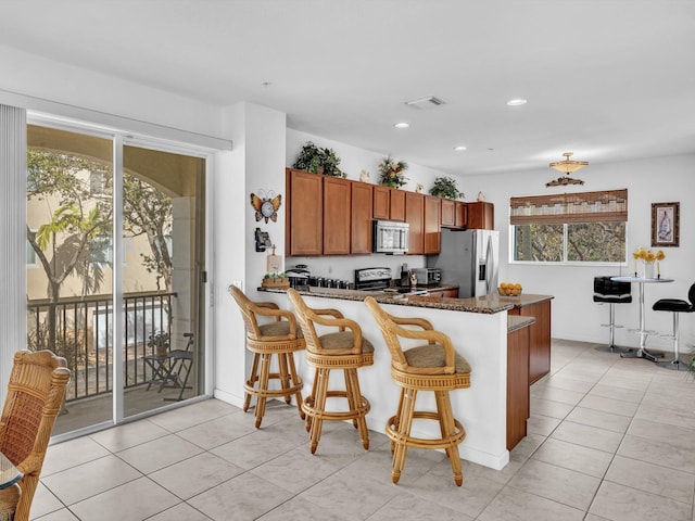 kitchen with stainless steel appliances, a breakfast bar, kitchen peninsula, and dark stone counters