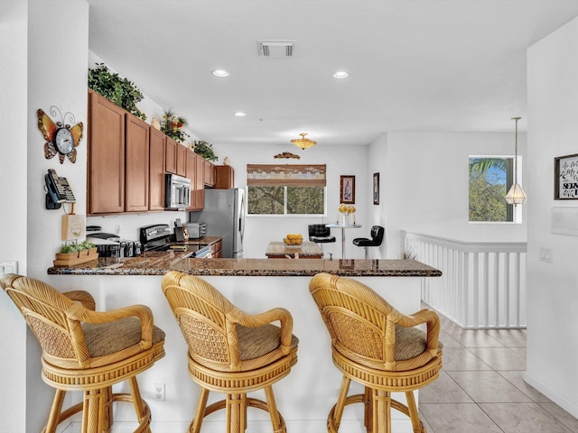 kitchen with a kitchen bar, hanging light fixtures, light tile patterned floors, kitchen peninsula, and stainless steel appliances