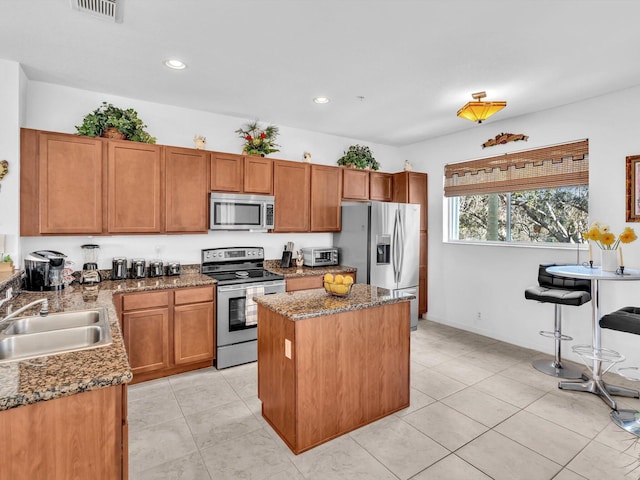 kitchen with sink, light tile patterned floors, appliances with stainless steel finishes, dark stone countertops, and a kitchen island