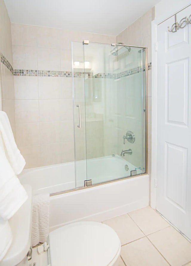 bathroom with tile patterned flooring, bath / shower combo with glass door, and toilet