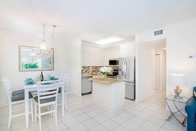 kitchen with a kitchen island, appliances with stainless steel finishes, decorative light fixtures, white cabinetry, and light stone counters