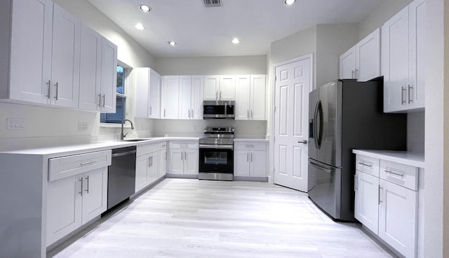 kitchen with stainless steel appliances, sink, light hardwood / wood-style flooring, and white cabinets