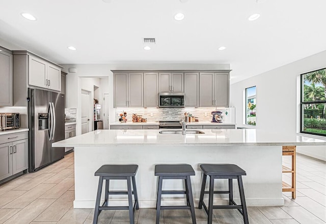 kitchen with gray cabinetry, a sink, visible vents, appliances with stainless steel finishes, and backsplash