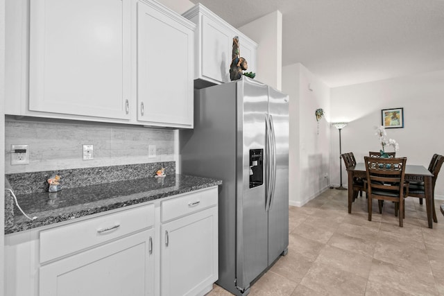 kitchen featuring stainless steel fridge, dark stone counters, baseboards, white cabinetry, and decorative backsplash