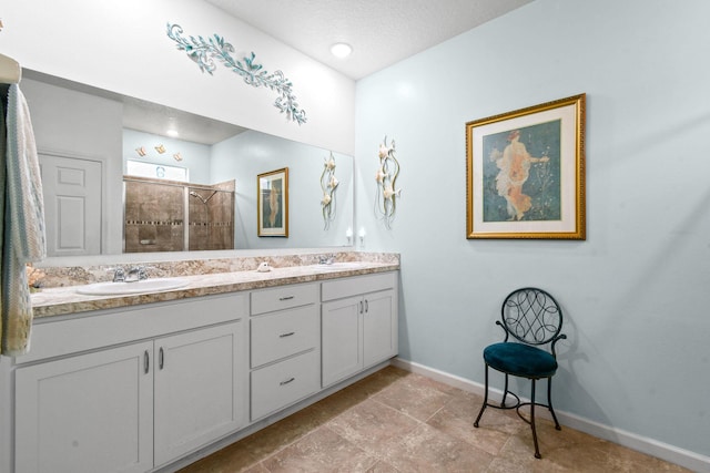 bathroom featuring baseboards, double vanity, a stall shower, and a sink