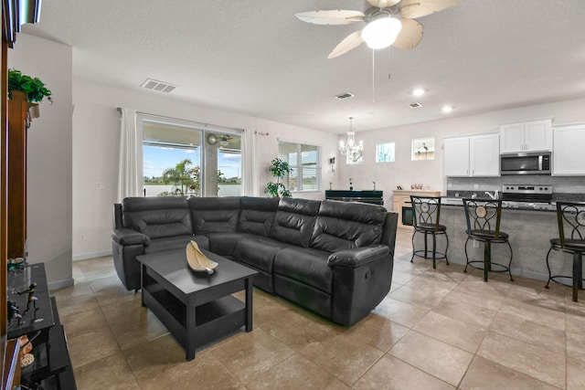 living area with a textured ceiling, visible vents, light tile patterned floors, and ceiling fan with notable chandelier