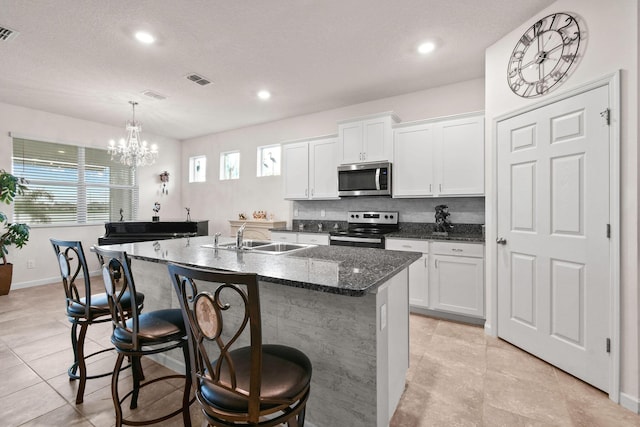 kitchen featuring white cabinets, an island with sink, stainless steel appliances, a sink, and a kitchen bar