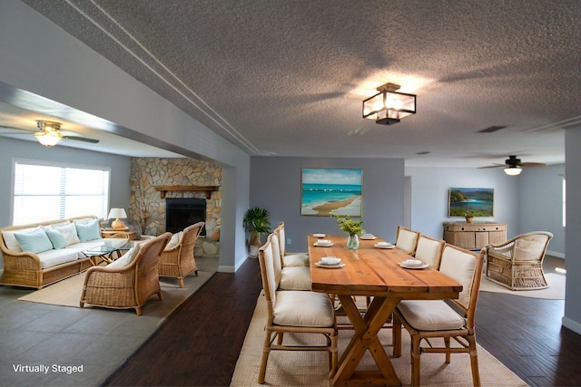 dining space with wood finished floors, a textured ceiling, a fireplace, and ceiling fan