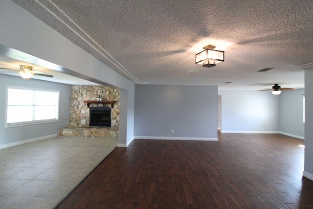 unfurnished living room with a stone fireplace, baseboards, ceiling fan, and dark wood finished floors