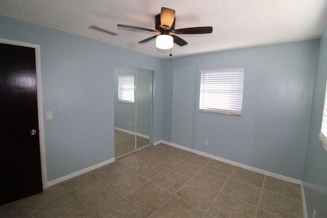 unfurnished bedroom featuring tile patterned floors, a textured ceiling, baseboards, visible vents, and ceiling fan