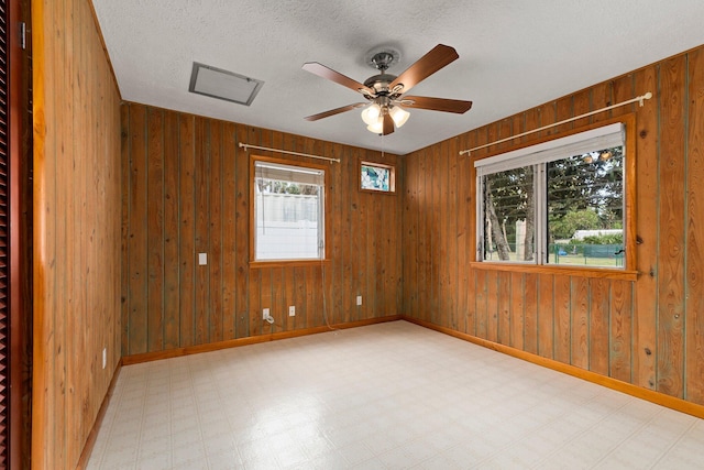 unfurnished room with ceiling fan, a healthy amount of sunlight, a textured ceiling, and wood walls