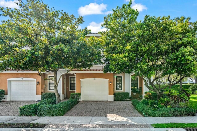 view of front of house with decorative driveway, a tile roof, an attached garage, and stucco siding