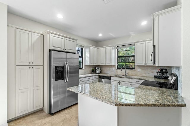 kitchen with decorative backsplash, appliances with stainless steel finishes, a sink, light stone countertops, and a peninsula