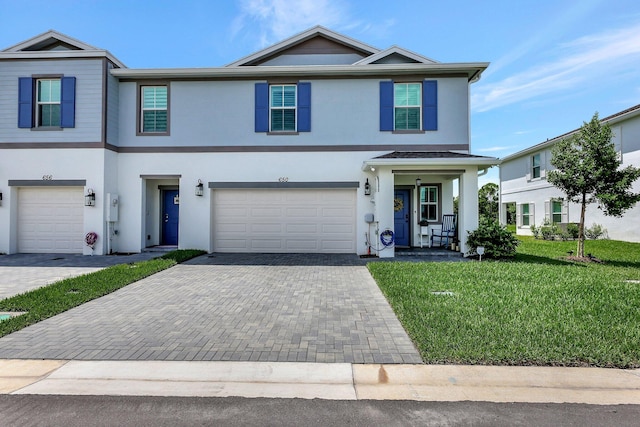 view of front of property with a garage, decorative driveway, a front lawn, and stucco siding