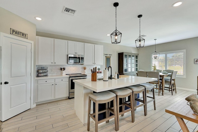 kitchen with wood finish floors, tasteful backsplash, visible vents, appliances with stainless steel finishes, and white cabinets