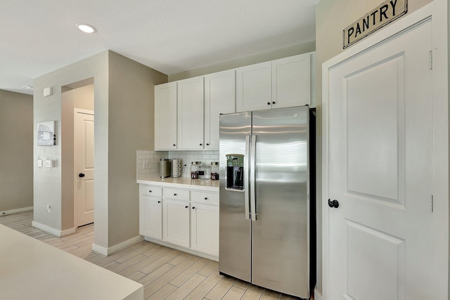 kitchen featuring white cabinets, light countertops, stainless steel refrigerator with ice dispenser, wood tiled floor, and tasteful backsplash