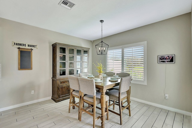 dining space with baseboards, visible vents, light wood finished floors, and an inviting chandelier