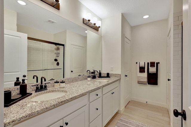 bathroom with double vanity, visible vents, a sink, a shower stall, and wood finished floors