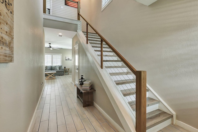 staircase featuring wood finish floors, baseboards, ceiling fan, and a high ceiling