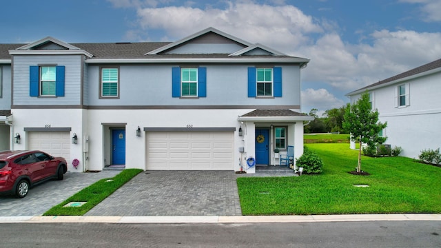 view of property with a front lawn, decorative driveway, an attached garage, and stucco siding