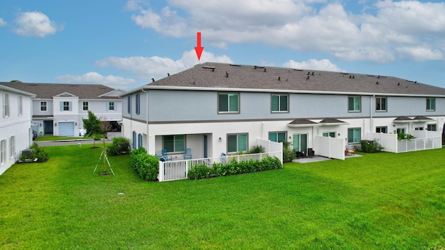 rear view of house with a yard, fence, and stucco siding