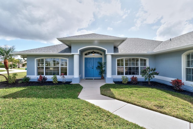 view of exterior entry featuring roof with shingles, a lawn, and stucco siding