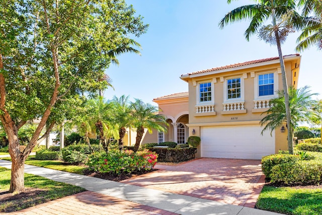 mediterranean / spanish home featuring decorative driveway, an attached garage, a tile roof, and stucco siding