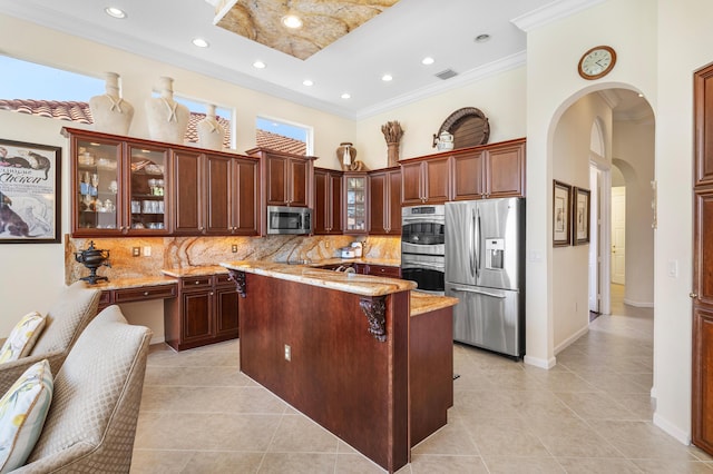 kitchen with a center island with sink, arched walkways, decorative backsplash, a towering ceiling, and appliances with stainless steel finishes