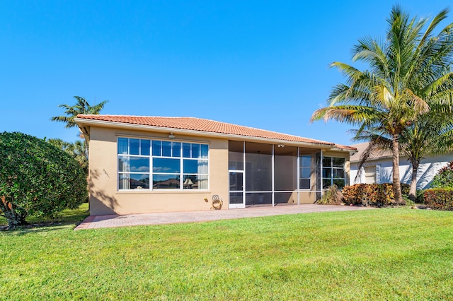 rear view of property featuring a sunroom, a tile roof, a lawn, and stucco siding