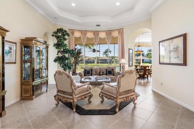 living room with light tile patterned floors, a tray ceiling, baseboards, and crown molding